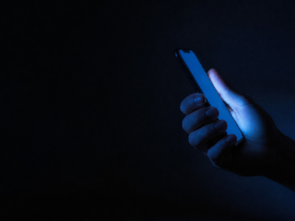 Adolescente usa su teléfono celular de noche, con el rostro iluminado por la pantalla"
